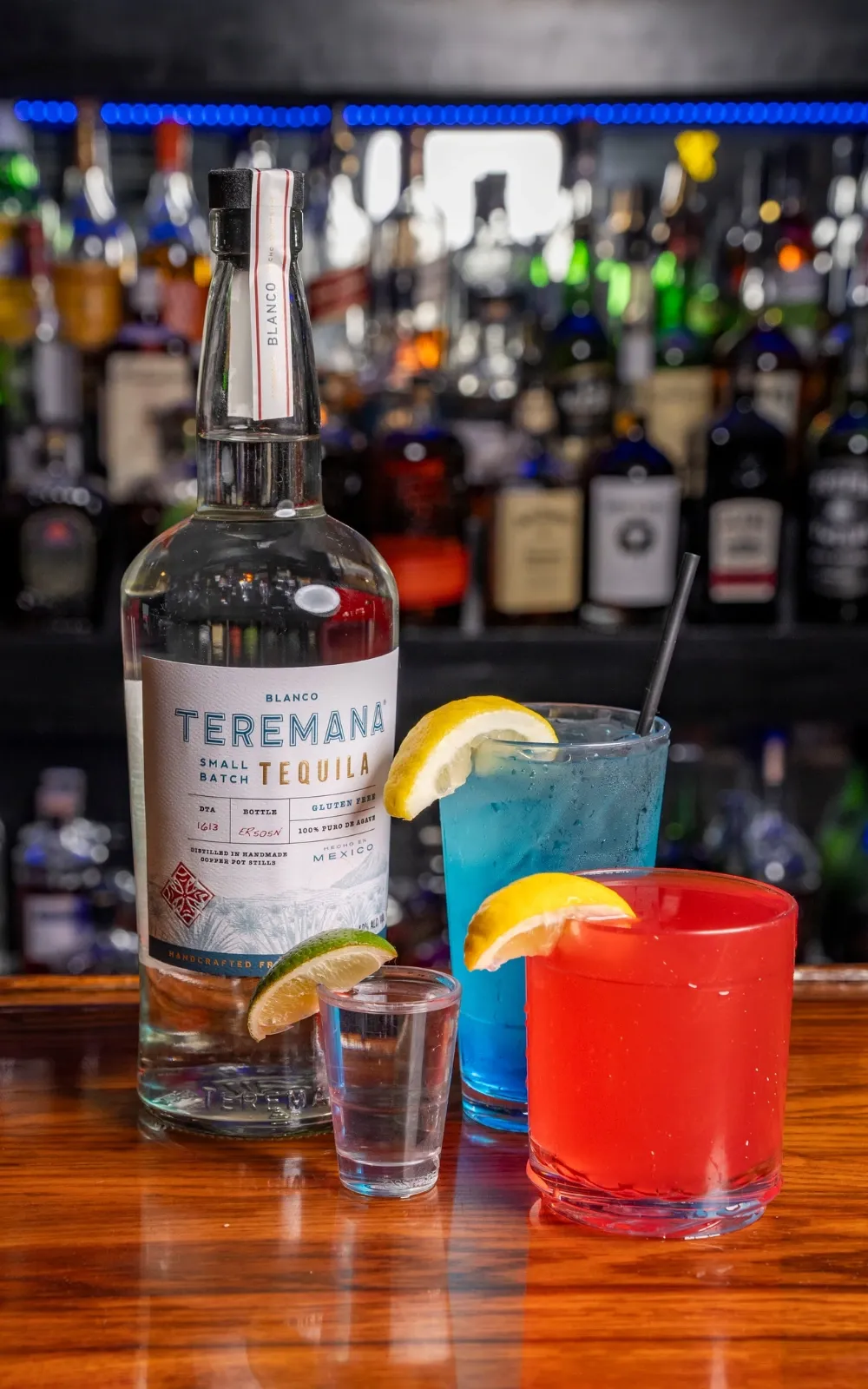 A bottle of tequila with cocktails and a shot on the bar